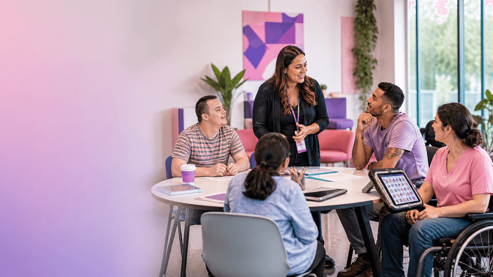 Diverse group, including a wheelchair user, smiling and collaborating around a table in an office.