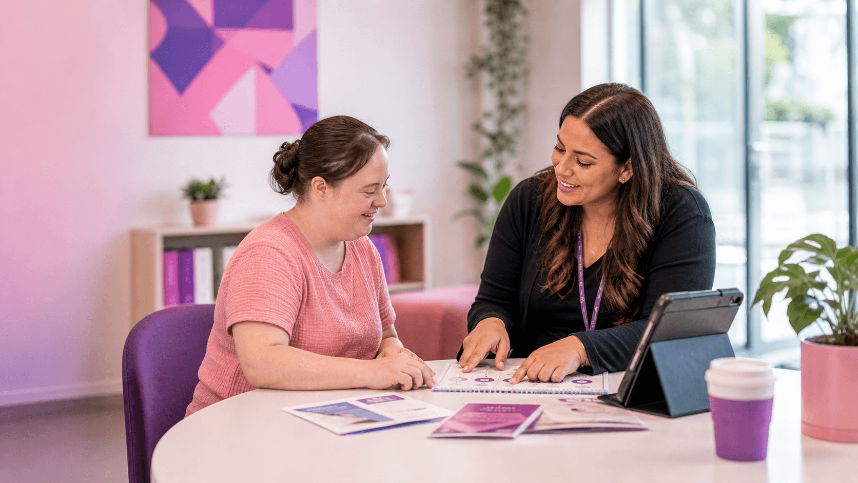 Woman with Down syndrome and a support worker smiling while reviewing documents at a table.