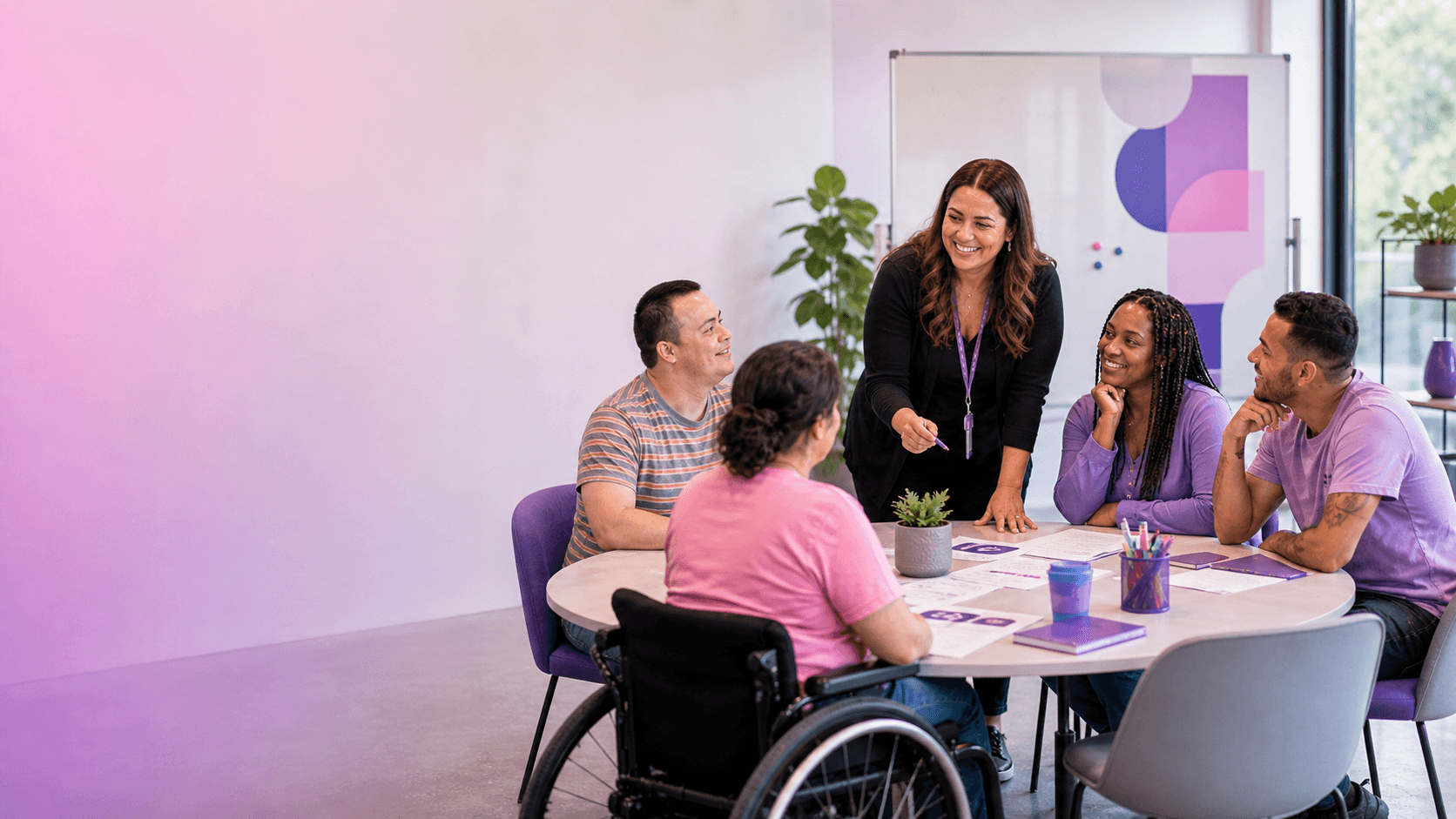Diverse colleagues, including a wheelchair user, smiling and collaborating around a round office table.