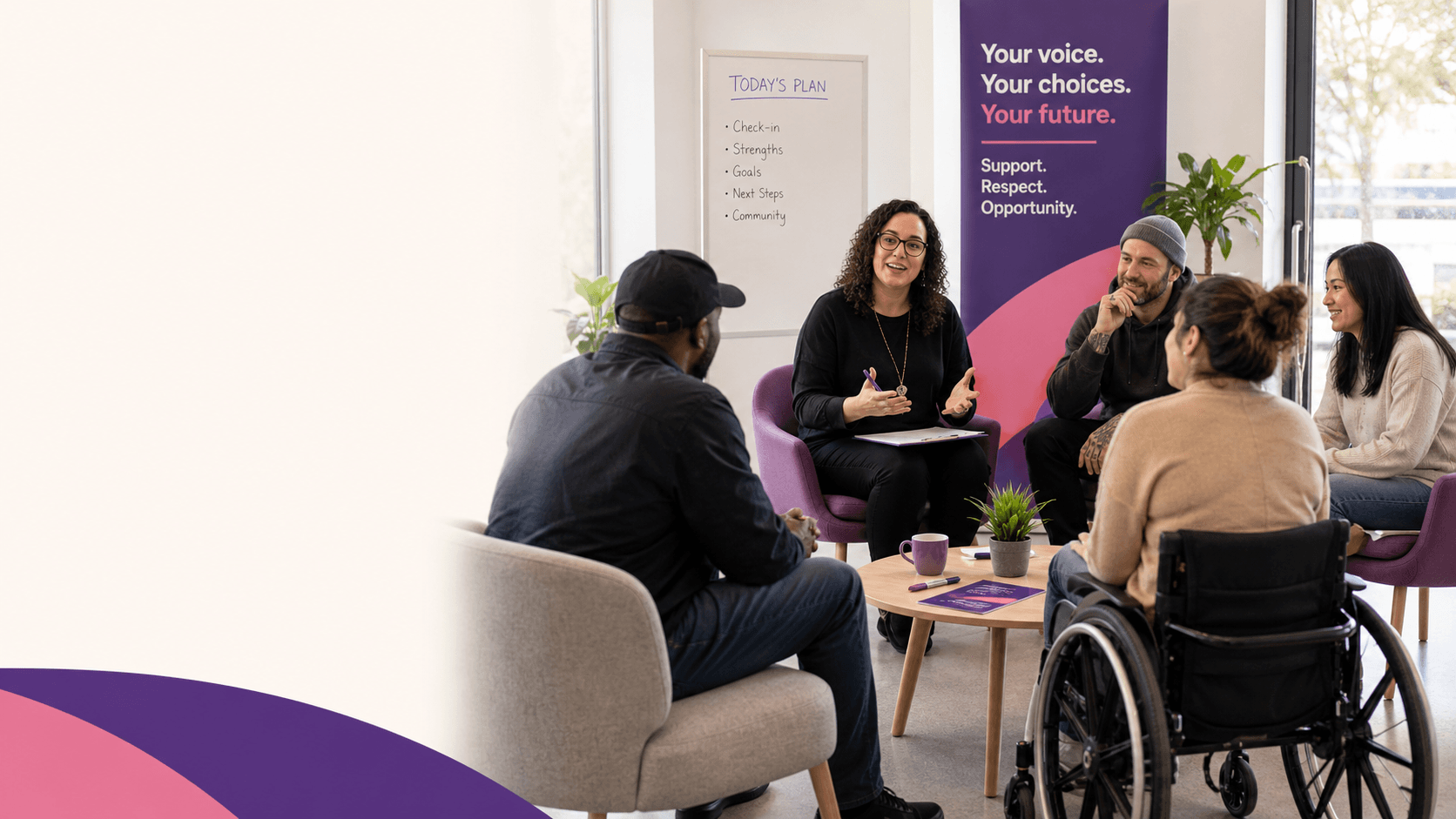 Diverse group of people, including a wheelchair user, listening to a woman leading a meeting.