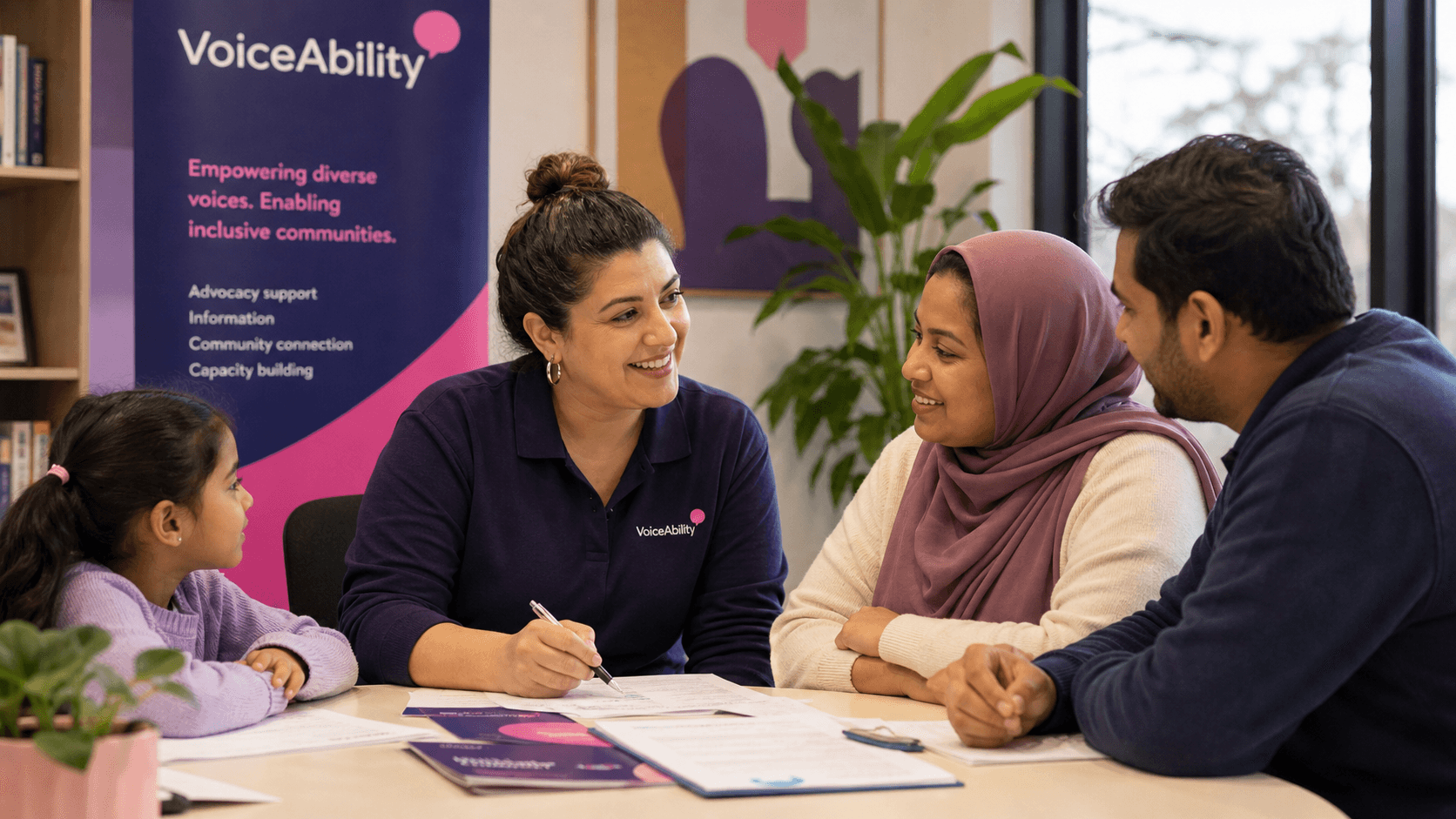 VoiceAbility staff member smiling while assisting a diverse family with paperwork at a table.