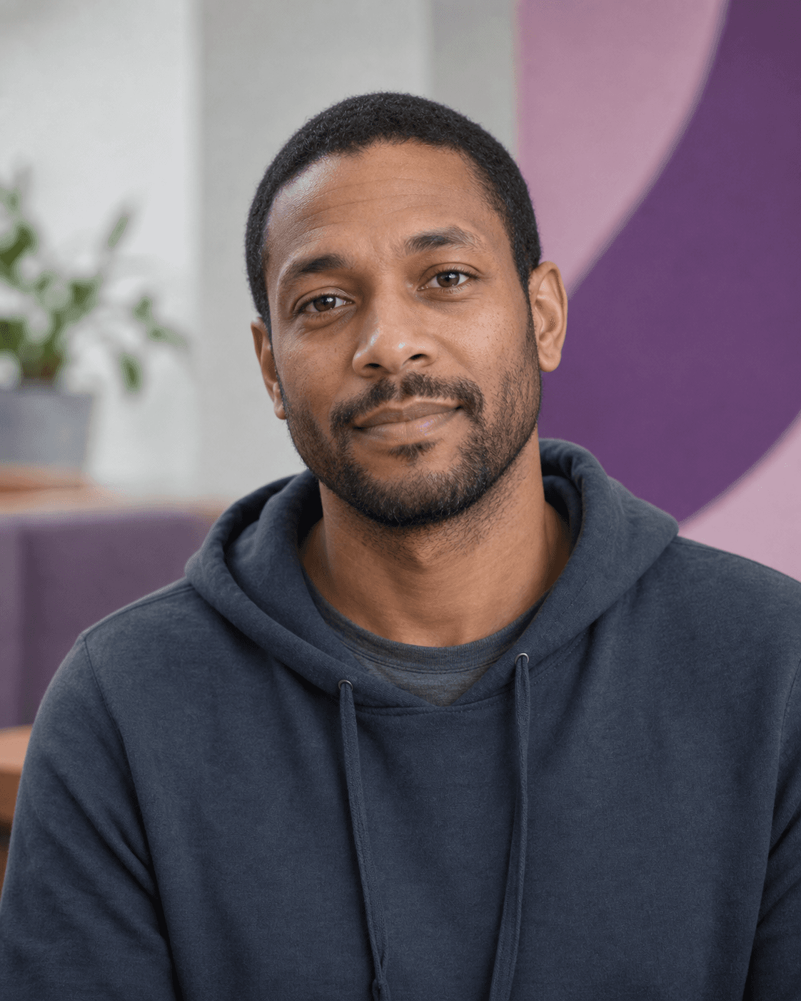 Portrait of a Black man with short hair and a beard wearing a grey hoodie.
